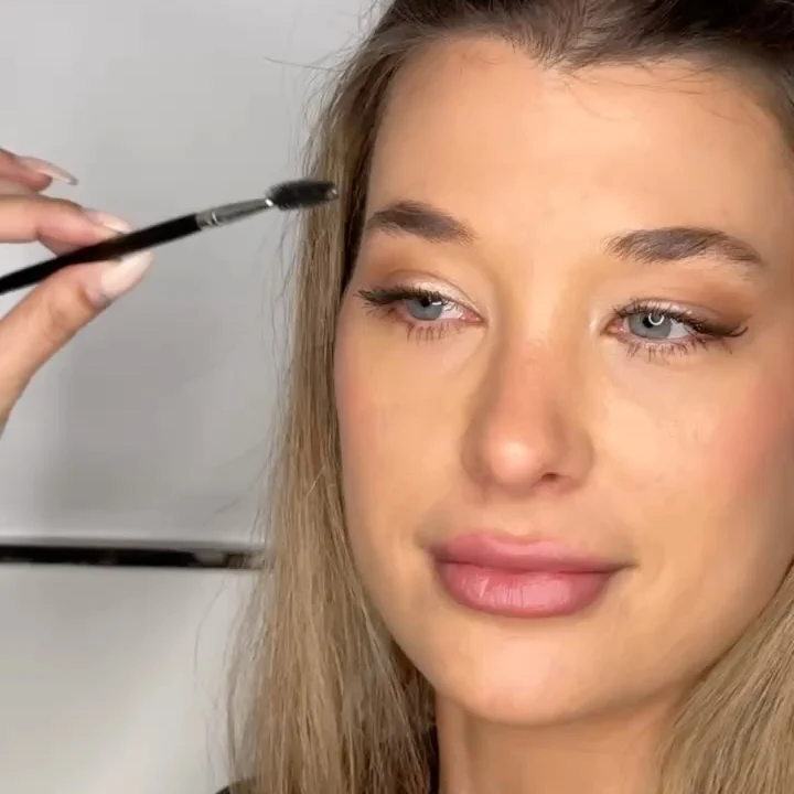 Mujer rellenándose las cejas con un pincel frente al espejo